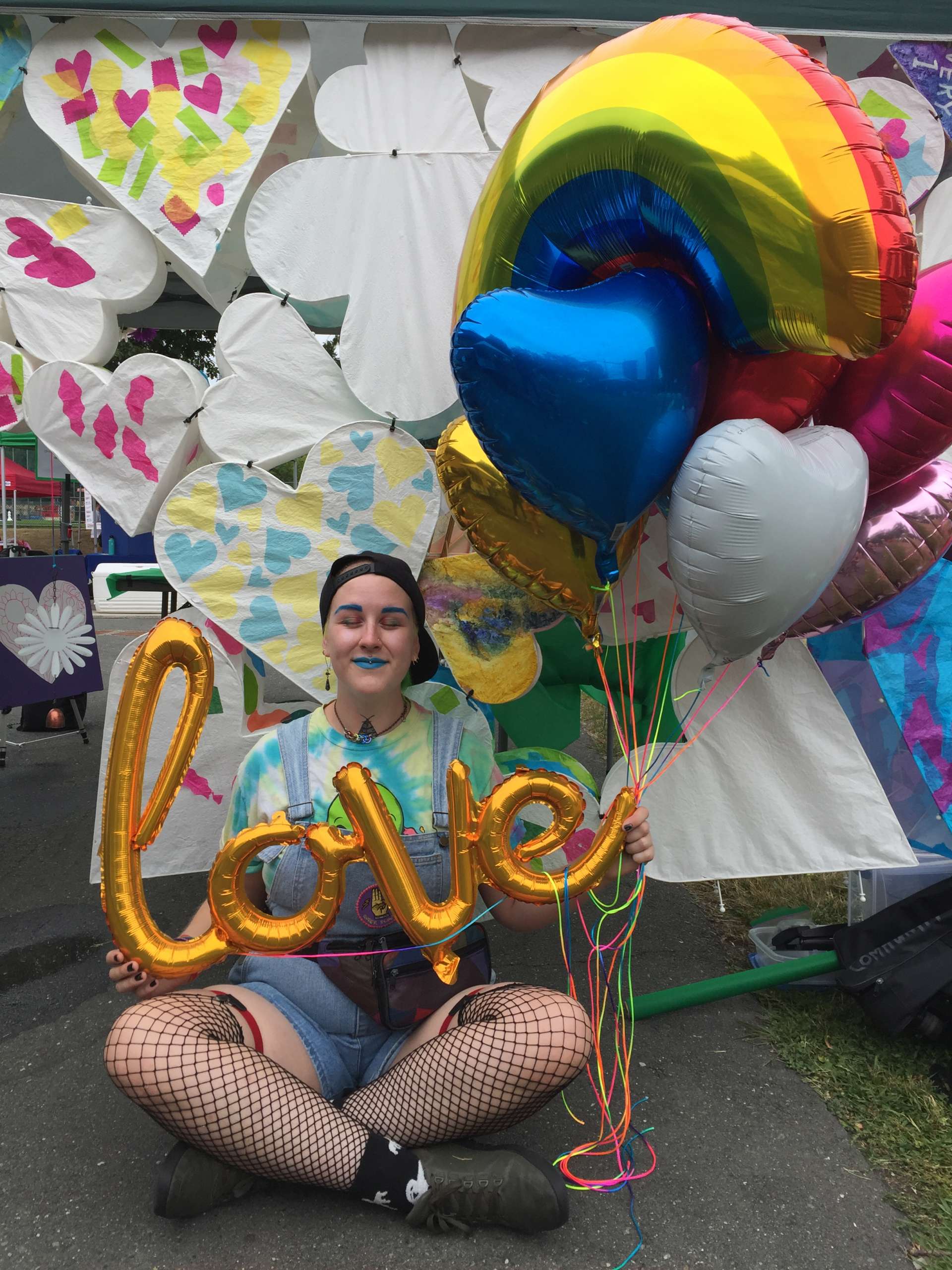 a person sitting on the ground holding a balloon that reads "love" and other coloured balloons