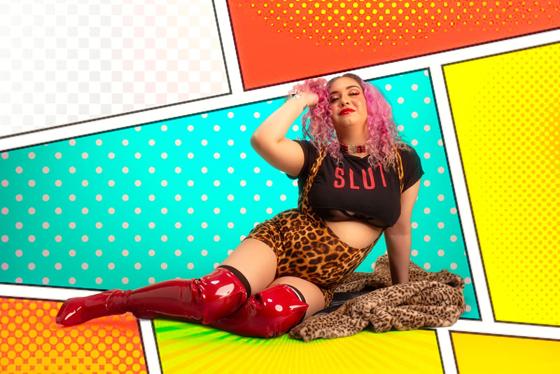 Photo of burlesque performer RainbowGlitz sitting on the ground with a comic style background